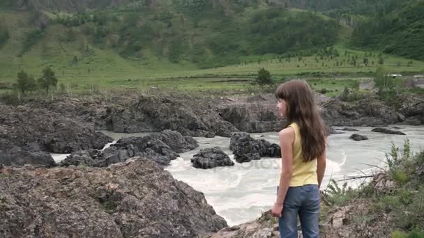 Liten flicka traveler. ett barn står på kanten av en klippa i en mountain river på en bakgrund av berg — Stockvideo
