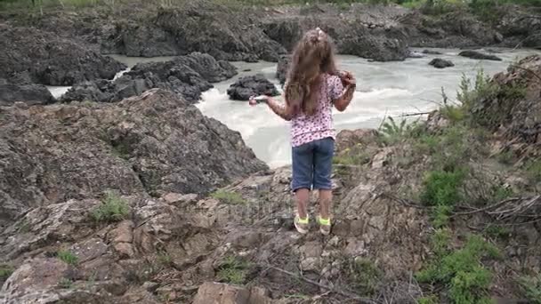 Маленькая девочка-путешественница. ребенок стоит на краю скалы в горной реке на фоне гор — стоковое видео