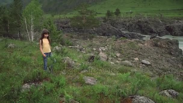 Lilla flickan promenerar längs en äng nära en mountain river. Barn turist på en resa på jakt efter äventyr — Stockvideo