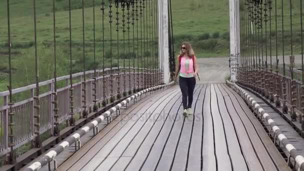 Meisje toerist met een rugzak loopt naar het avontuur. Jonge vrouw reiziger loopt langs de brug. — Stockvideo