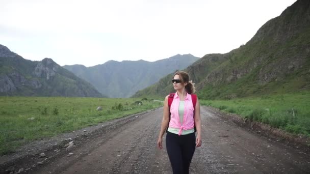 젊은 여자는 배낭에 산에서 비포장도로 따라가. 여자는 관광 모험을 향해 간다 — 비디오