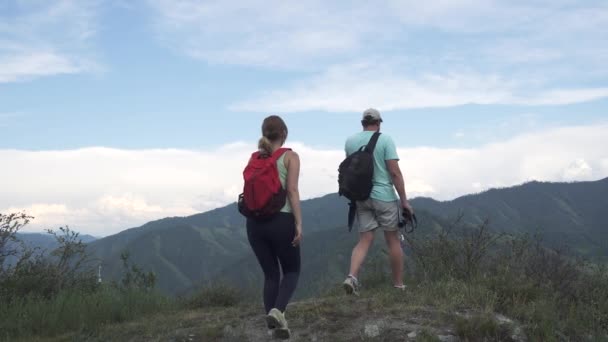 Hombre joven viajero mostrando a través de prismáticos el propósito de viajar a su novia. Turistas con mochilas en la cima de la montaña — Vídeo de stock