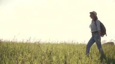 genç kız turistik bir çayır on gider. güneş gözlüğü, şapka ve bir sırt çantası giyen kadın Gezgin