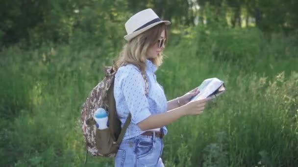 Chica turista con mapa en la mano caminando por un sendero forestal. viajera joven con una mochila . — Vídeo de stock