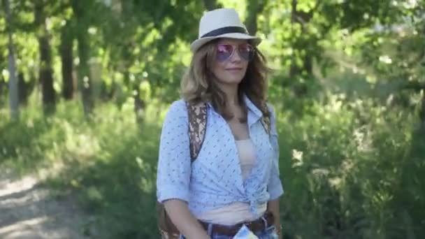 Retrato de una chica hipster con sombrero y gafas de sol. Mujer joven con una mochila — Vídeo de stock