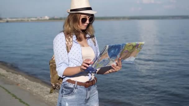 Путешественник с картой в руке. молодая привлекательная девушка с рюкзаком на фоне моря — стоковое видео