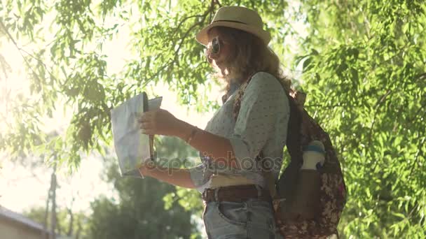 Girl es un turista elige un destino turístico en el mapa. mujer joven hipster con gafas de sol y un sombrero — Vídeo de stock