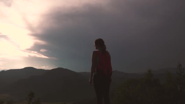 Девушка туристка на вершине горы. молодая женщина наслаждается закатом и потрясающими видами. путешественник с рюкзаком — стоковое видео