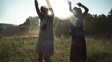 Kızlar hippi kıyafet dansında şafakta, üst ellerini yükselterek giyinmiş. ağır çekim