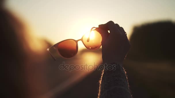Menina olha para o sol através de óculos de sol. mulher segura na mão óculos de sol. câmara lenta — Vídeo de Stock