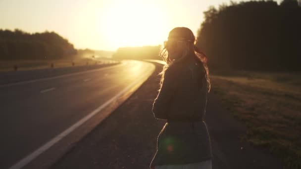 A rapariga está na estrada ao amanhecer. jovem mulher atraente em roupas hippie sorrindo e olhando para a câmera. câmara lenta — Vídeo de Stock