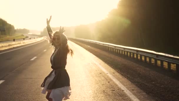 Dziewczyna w ubrania hippie działa na drodze o świcie. dziewczyna jest na drodze o świcie. Młoda atrakcyjna kobieta w ubrania hippie, uśmiechając się i patrząc na kamery. zwolnionym tempie — Wideo stockowe