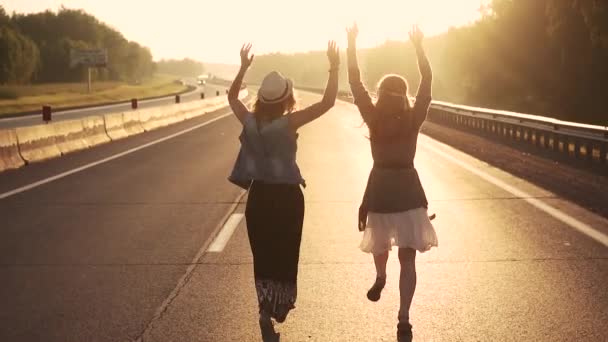 Mädchen im Hippie-Outfit auf einer einsamen Straße in den Strahlen der aufgehenden Sonne. Zeitlupe — Stockvideo