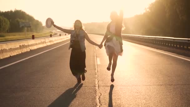 Mädchen im Hippie-Outfit auf einer einsamen Straße in den Strahlen der aufgehenden Sonne. Zeitlupe — Stockvideo