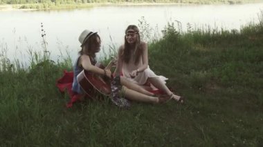 Hippi giysili kızlar gitar çalıp şarkı otururken Uçurumdaki Nehri yakınında