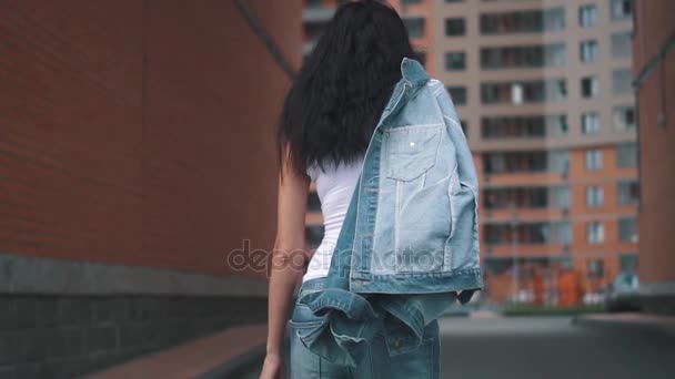 Joven chica atractiva disfrutando de un paseo por la calle. morena en jeans y camiseta caminando por la ciudad en un día de verano. cámara lenta — Vídeo de stock