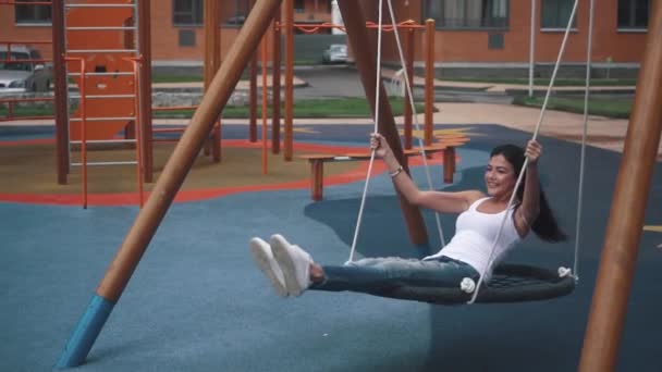 Молода жінка, розмахуючи на гойдалках гамаку на дитячому майданчику в місті. повільний рух — стокове відео