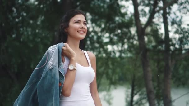 Jeune fille attrayante marchant dans un parc d'été. jeune femme en jean et un t-shirt blanc profitant d'une journée d'été en plein air. au ralenti — Video