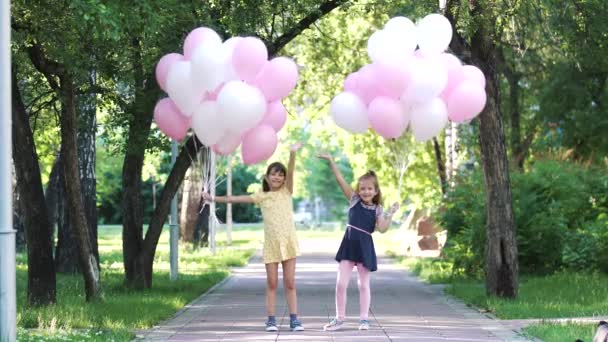 Dvě malé holčičky se drží hodně balonů, usmívat se a mávat rukou — Stock video