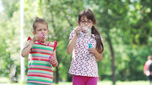 Niño feliz soplando burbujas de jabón en el parque de primavera. Dos niñas se divierten en el parque de verano. Movimiento lento — Vídeos de Stock