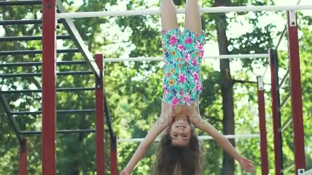 Little funny girl hanging upside down on the horizontal bar. slow motion — Stock Video