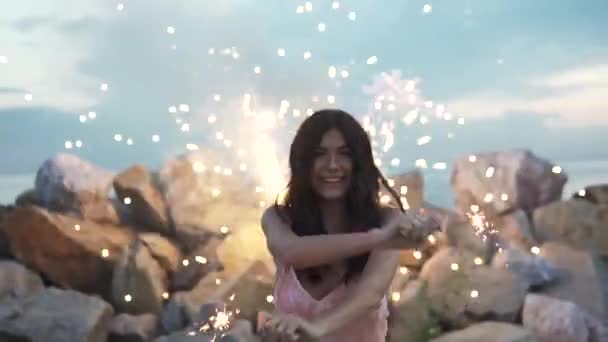 Portrait d'une fille joyeuse sur fond de feux d'artifice. Fille attrayante s'amuser et danser à une fête tenant bengale lumières. au ralenti — Video