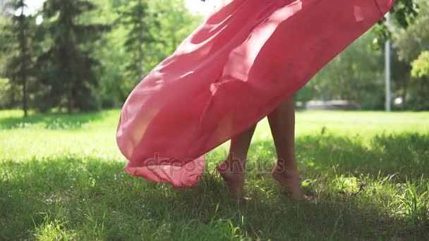 Pernas femininas fechadas. a menina no vestido vermelho e sapatos de salto alto está fugindo no beco verde em Park. câmara lenta — Vídeo de Stock