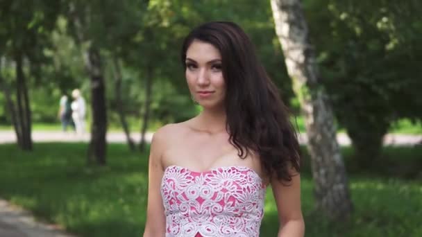 Retrato de cerca de una chica con apariencia oriental. chica atractiva en vestido elegante en un parque de verano sobre un fondo de árboles verdes — Vídeos de Stock