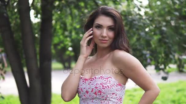 Close-up πορτρέτο ενός κοριτσιού με ανατολική εμφάνιση. ελκυστικό κορίτσι στο κομψό φόρεμα σε ένα πάρκο καλοκαίρι σε ένα φόντο από καταπράσινα δέντρα — Αρχείο Βίντεο