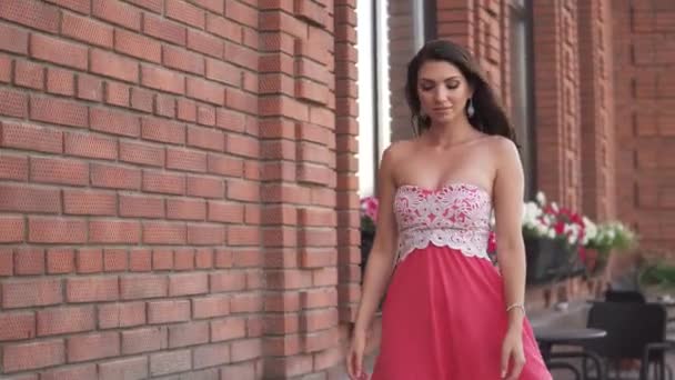 Девушка в красном платье идет по улице под заходящим солнцем — стоковое видео