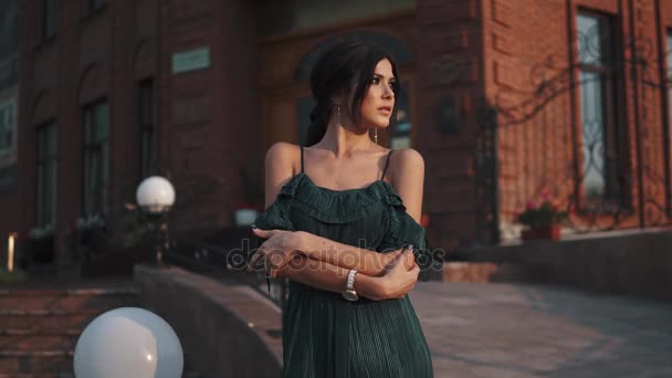 Portrait of beautiful girl with evening makeup and hairstyle. cute brunette posing for the camera at sunset on the background of the city — Stock Video