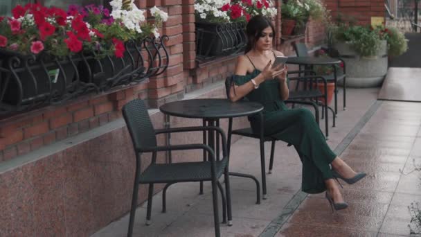 Charming girl uses a mobile phone sitting in a cafe outdoors in old town — Stock Video