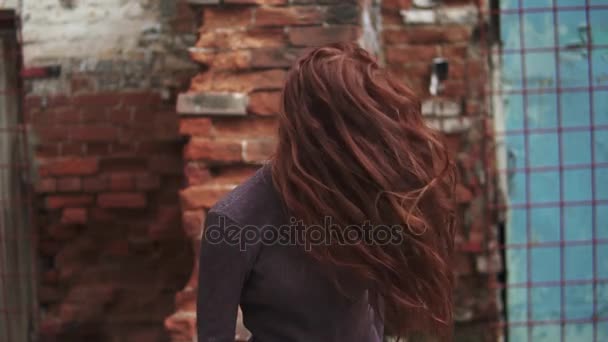 Rudowłosa dziewczyna jest imponująco zwracając się do kamery. Włosów łopocze na wietrze. Piękna młoda dziewczyna z piegami na tle budynku dawnej. zwolnionym tempie — Wideo stockowe