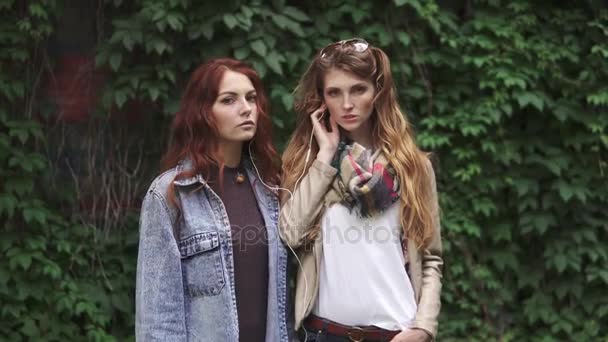 Portrét dvou dívek zrzavá, kteří poslouchat hudbu ve sluchátkách. Krásná přítelkyně s pihy pózuje na kameře. 20s — Stock video
