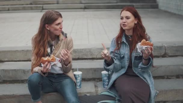 Två flickvänner äter hamburgare utomhus. 20s — Stockvideo