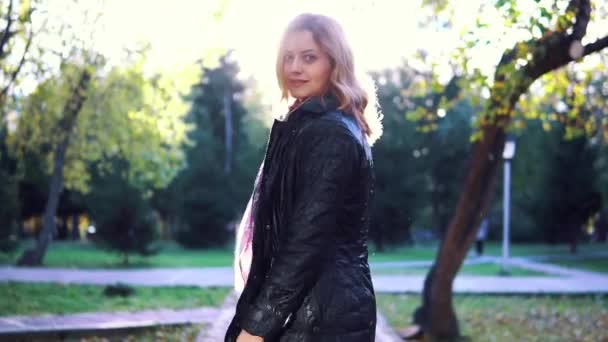 Retrato de mujer joven en el parque de otoño. la chica de la bufanda y el abrigo se gira juguetonamente y mira a la cámara. cámara lenta — Vídeos de Stock