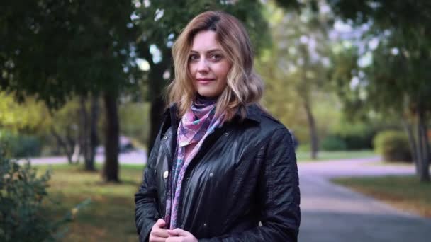 Primer plano retrato de mujer joven atractiva en el parque de otoño. chica en chaqueta y bufanda — Vídeo de stock