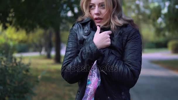 The girl froze in the autumn Park. young woman wrapped in a scarf and breathes on his hands to warm them up — Stock Video
