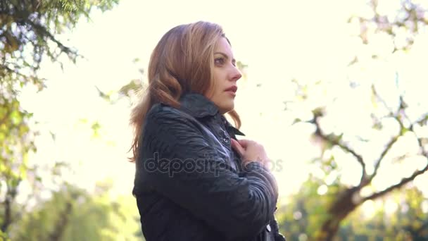 Retrato de una mujer fría en un parque de otoño. la chica estornuda y se envuelve en una bufanda — Vídeos de Stock