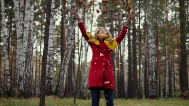 genç kadın düşen sarı yapraklar ve having fun atar. Kız sonbahar ormanın içinde kırmızı paltolu. ağır çekim