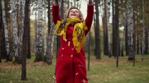 Attraente giovane donna getta foglie gialle che cadono. ragazza che cammina in autunno Parco in trench. rallentatore — Video Stock