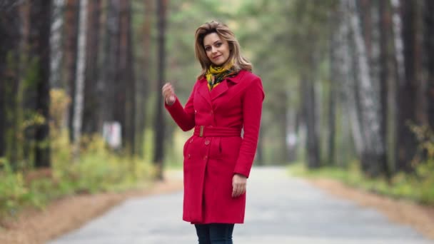 Портрет молодой женщины в осеннем парке. красивая девушка в красном пальто позирует и улыбается в камеру — стоковое видео