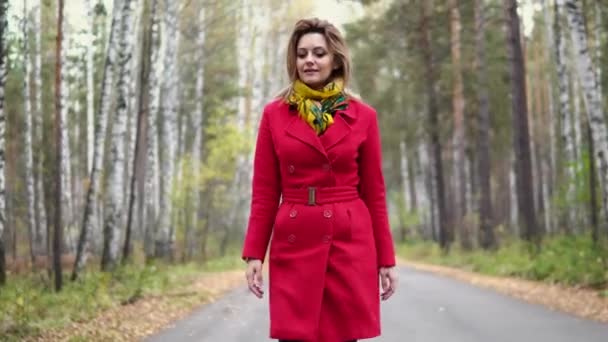 秋の公園を歩いて魅力的な若い女性。赤いコートとスカーフの女の子 — ストック動画
