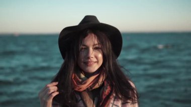 Sahilde genç bir kadın portresi. Kız gülümseyerek ve su kamera poz şapka ve sonbahar ceket. Ağır çekim