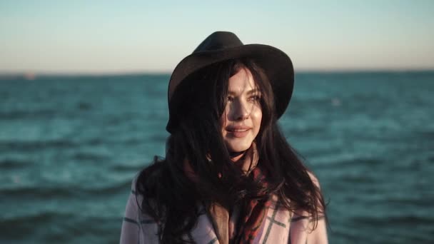 Sahilde genç bir kadın portresi. Kız gülümseyerek ve su kamera poz şapka ve sonbahar ceket. Ağır çekim — Stok video