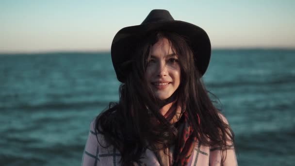 Retrato de linda chica primer plano sobre el fondo del mar. mujer joven en abrigo de otoño y sombrero posando y sonriendo a la cámara.. Movimiento lento — Vídeos de Stock