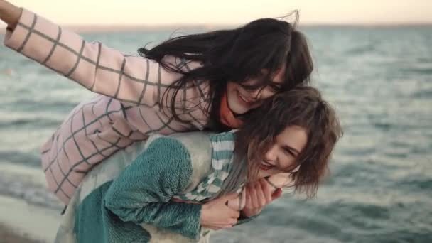 Two young attractive girls have fun and embrace. best friends spend time together outdoors by the water. portrait of girlfriends on the beach at sunset — Stock Video