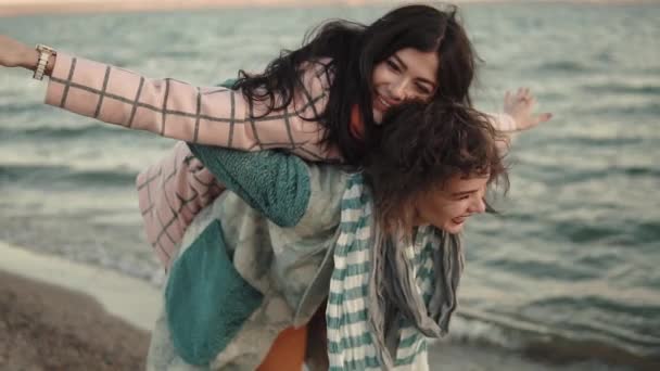 Дві молоді привабливі дівчата розважаються і обіймаються. найкращі друзі проводять час разом на відкритому повітрі біля води. портрет дівчат на пляжі на заході сонця — стокове відео
