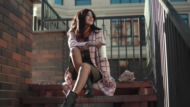 Smiling young woman drinking coffee in the city. fashionable girl in an autumn coat — Stock Video