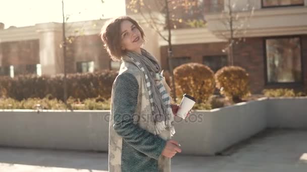 Portret młodej dziewczyny w jesienny płaszcz w bezpośrednim świetle słonecznym. piękna młoda kobieta z bukiet kwiatów pozowanie i uśmiechając się do kamery — Wideo stockowe